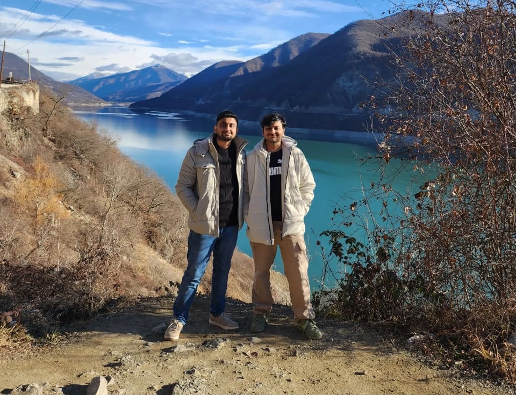 The two founders standing on a mountain path above a turquoise lake.